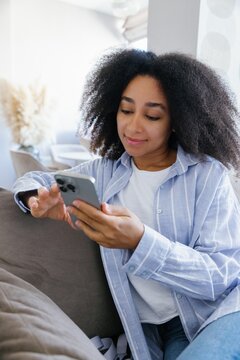 Young black woman watching mobile phone on couch at living room