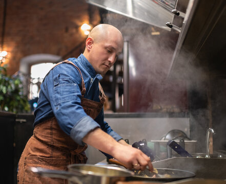 Bald male chef frying dish in cafe