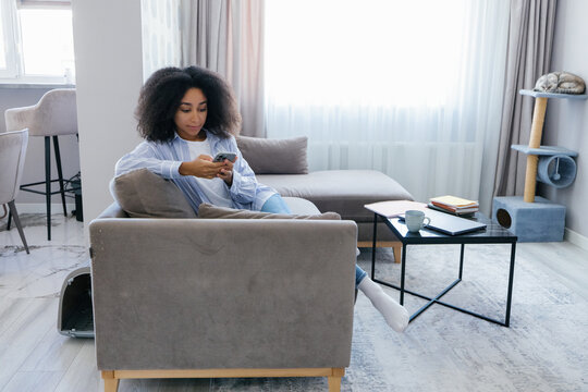 Young focused black woman using and watching cellphone on sofa