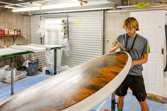 Shaper brushing resin on surfboard rail
