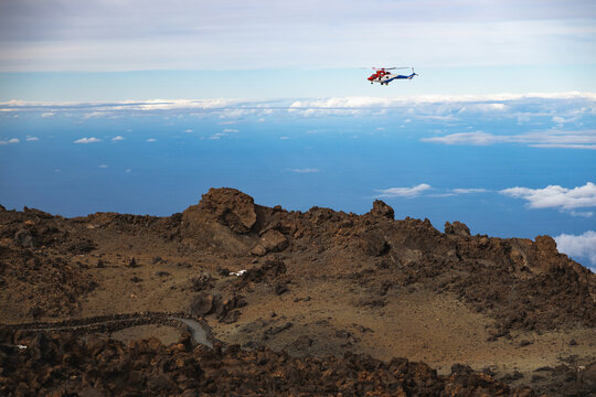 Red rescue helicopter flying above mountains and clouds.