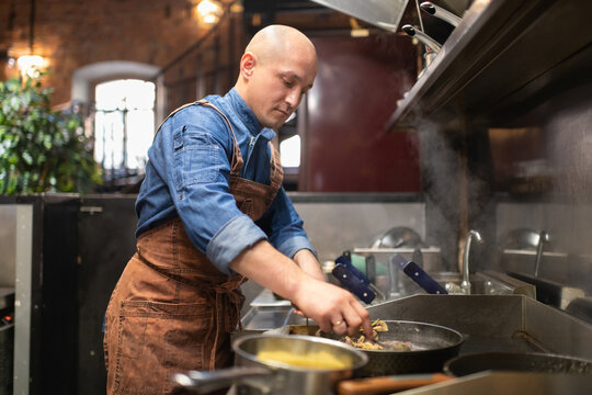 Bald man frying food in cafeteria kitchen