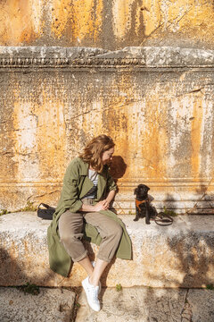 Woman sitting with puppy by ancient wall 