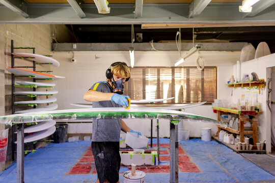 Shaper spreading resin on surfboard in Australia