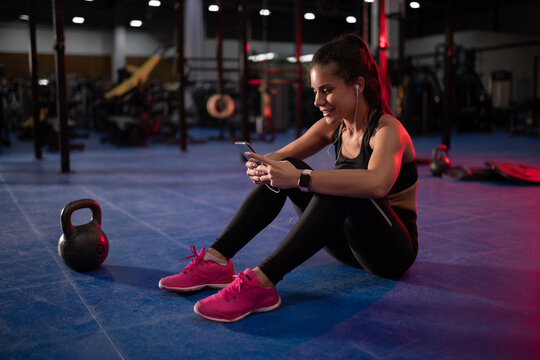 Cheerful sportswoman listening to music and using smartphone in gym