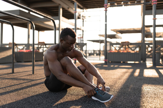 Concentrated black man tying sneaker on playground