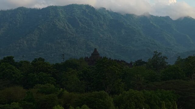 Aerial view of Borobudur Temple surrounded by lush tropical forest with misty mountains and clouds in the background Kecamatan Borobudur, Jawa Tengah, Indonesia.