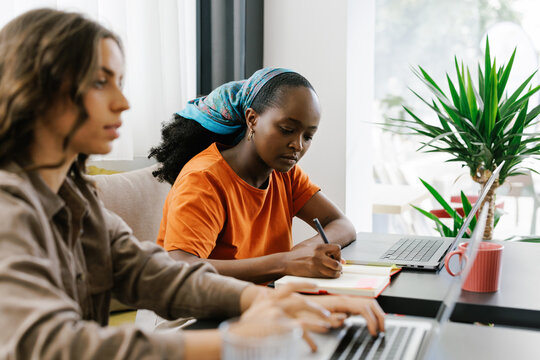 Two Women Working at a Table in a Bright Cafe Using Laptop