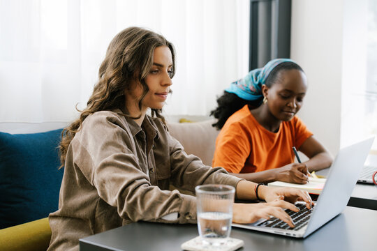 Two Women Working at a Table in a Bright Cafe Using Laptop