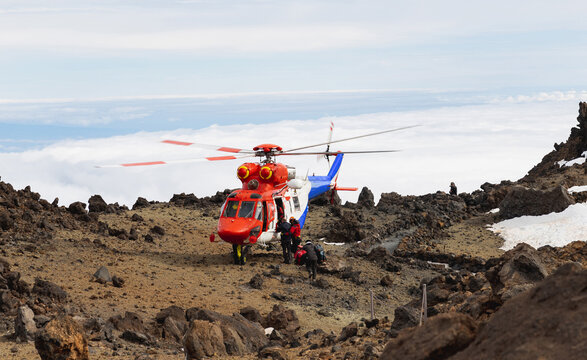 Red rescue helicopter flying above mountains and clouds.