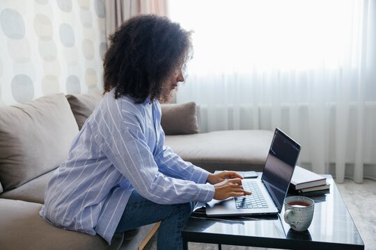 Side view of black woman typing laptop on sofa at table at home