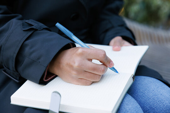 Partial black female entrepreneur writing in copybook on bench