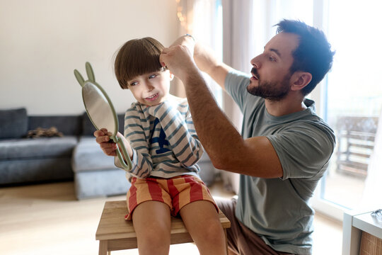 Father cutting son&rsquo;s hair while boy looks in mirror