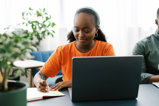Young Woman Writes in Notebook While Working on Laptop in Office