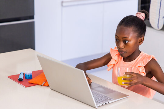 African American child working at kitchen counter using laptop holding orange juice, copy space