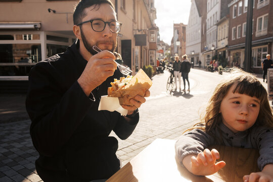 man eating kebab at german restaurant in city with his daughter beside