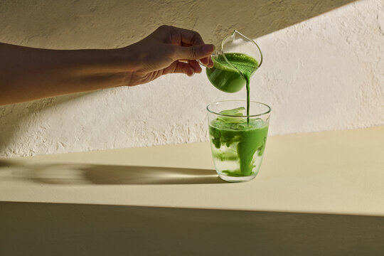A person elegantly pours green tea into a coconut water