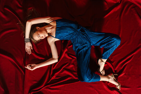 Top View Fashion Woman in Blue Jumpsuit Lying on Red Fabric 