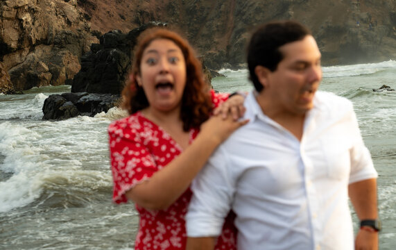 funny Couple Reacting with Surprise to Ocean Waves on Beach