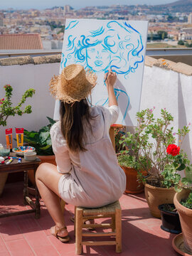 Woman Painting on a Terrace With City View and Potted Plants