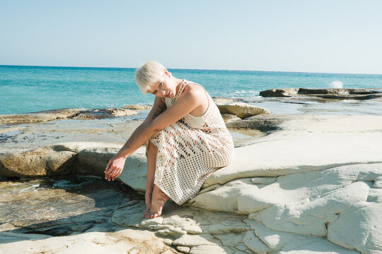 Woman Sits on Rocks by the Sea During Sunny Day