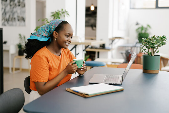 Woman Enjoys a Warm Drink While Working on a Laptop in an Office Space