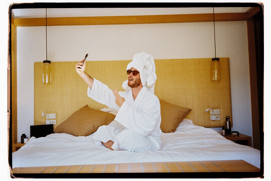 Man Taking a Selfie in Hotel Bed wearing a robe and a Head Towel