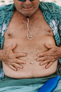 Mature Man Holding His Belly at the Beach on Sunny Day 
