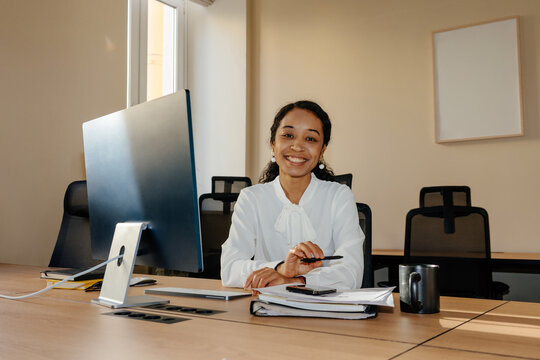 Smiling Businesswoman Sitting at Office Desk Looking at Camera