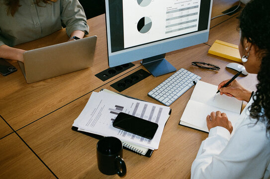 Businesswoman Taking Notes While Reviewing Financial Charts at Office 