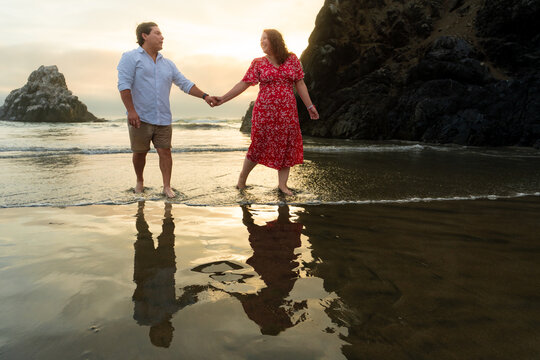 Young Couple Walking Hand in Hand on Beach at Golden Sunset