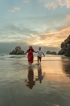 Young Couple Walking Hand in Hand on Beach at Golden Sunset
