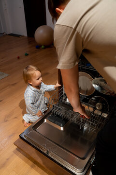 Father unloading dishwasher while toddler watches in kitchen