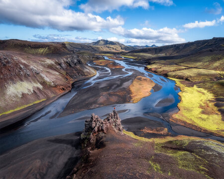 Hiker on lava rock overlooking glacial river valley, Iceland