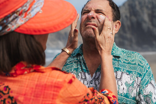 Woman Applying Sunscreen on Man's Face at Beach on Sunny Day