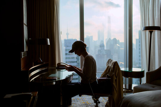 Person Sits at Desk in Hotel Room While Reading in City