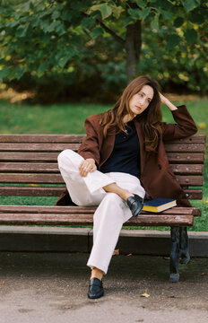 Woman Sits on a Bench Reading a Book in a Park During Daytime