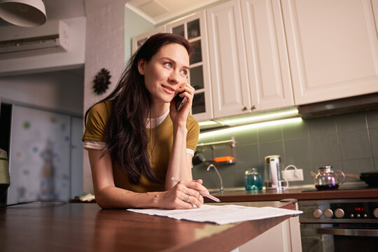 Woman talking on phone and writing in kitchen