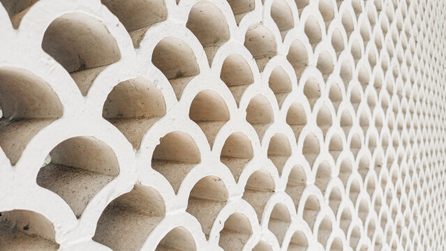 White breeze block wall with a repetitive curved pattern. Modern geometric concrete ventilation roster texture for background