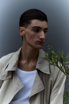 Young man in trench coat standing in profile against grey wall