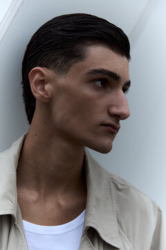 Young man in trench coat standing in profile against grey wall