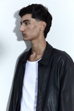 Young man wearing black leather jacket standing against white wall