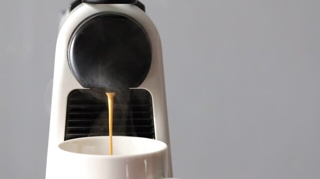Close-up video of a modern single-serve capsule coffee machine brewing a hot cup of fresh espresso at home