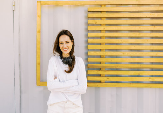 Woman Stands With Headphones by Wooden Wall in Urban Space