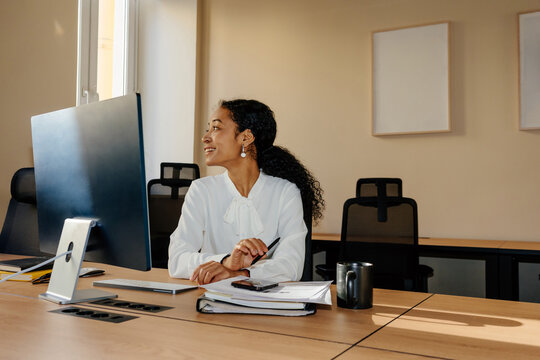 Smiling Businesswoman Sitting at Desk Working on Computer in Office