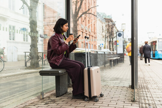 Young woman sitting at tram stop checking smartphone