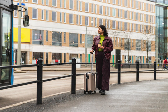 Young woman walking with suitcase on city street sidewalk