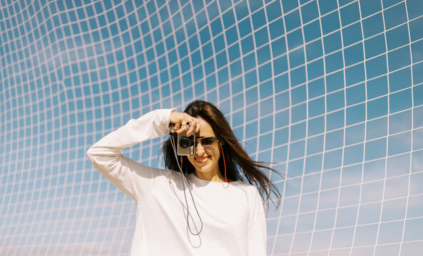 Woman Takes Picture With Camera Against Blue Sky and Grid Pattern