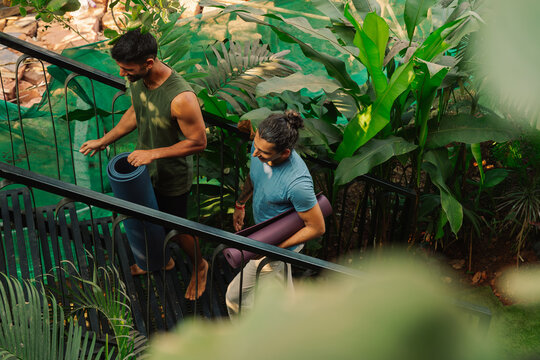 Two Men Walk Down Stairs With Yoga Mats in Tropical Garden