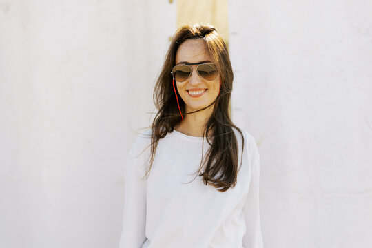 Woman Smiling With Sunglasses Near a White Wall in Daylight